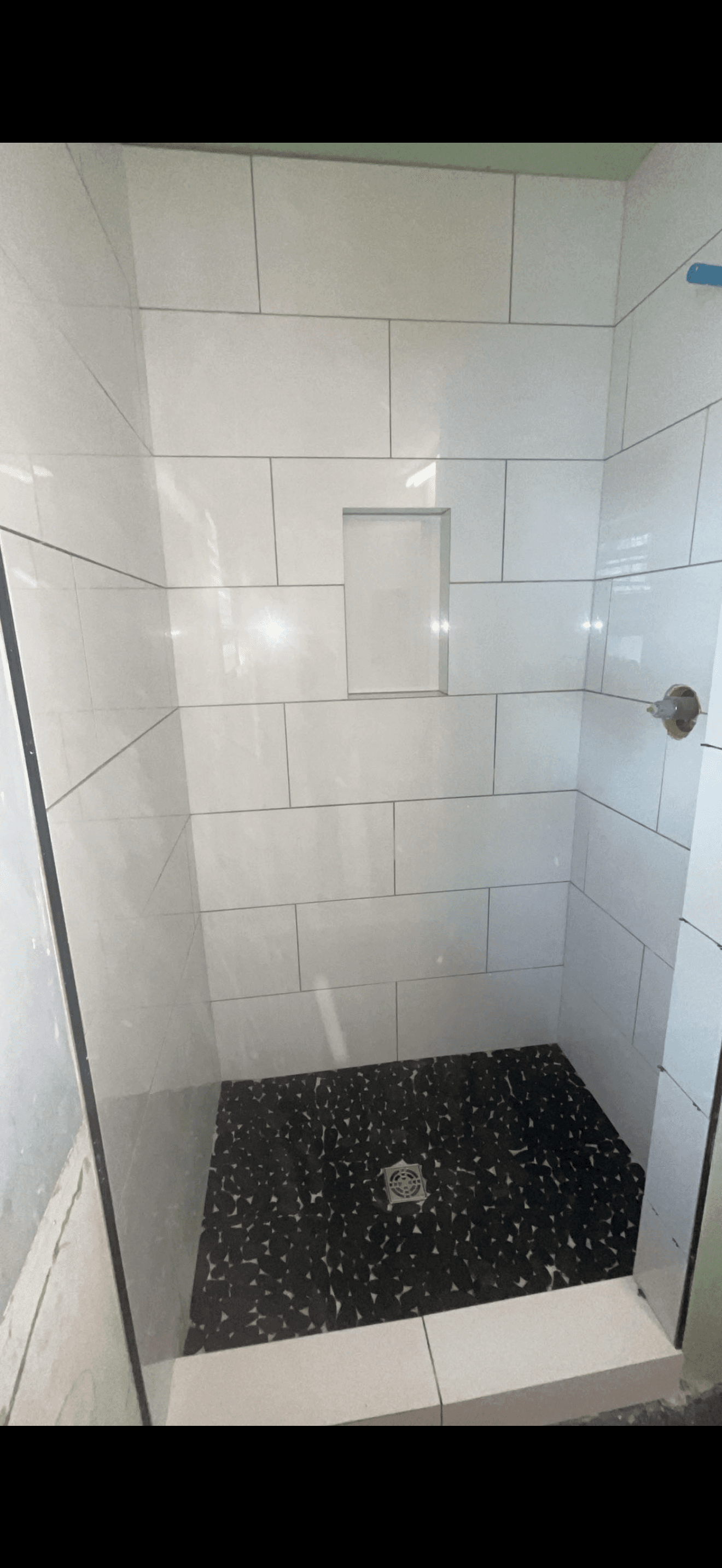 Walk-in shower with white tiled walls, a recessed niche, and a dark pebble floor.