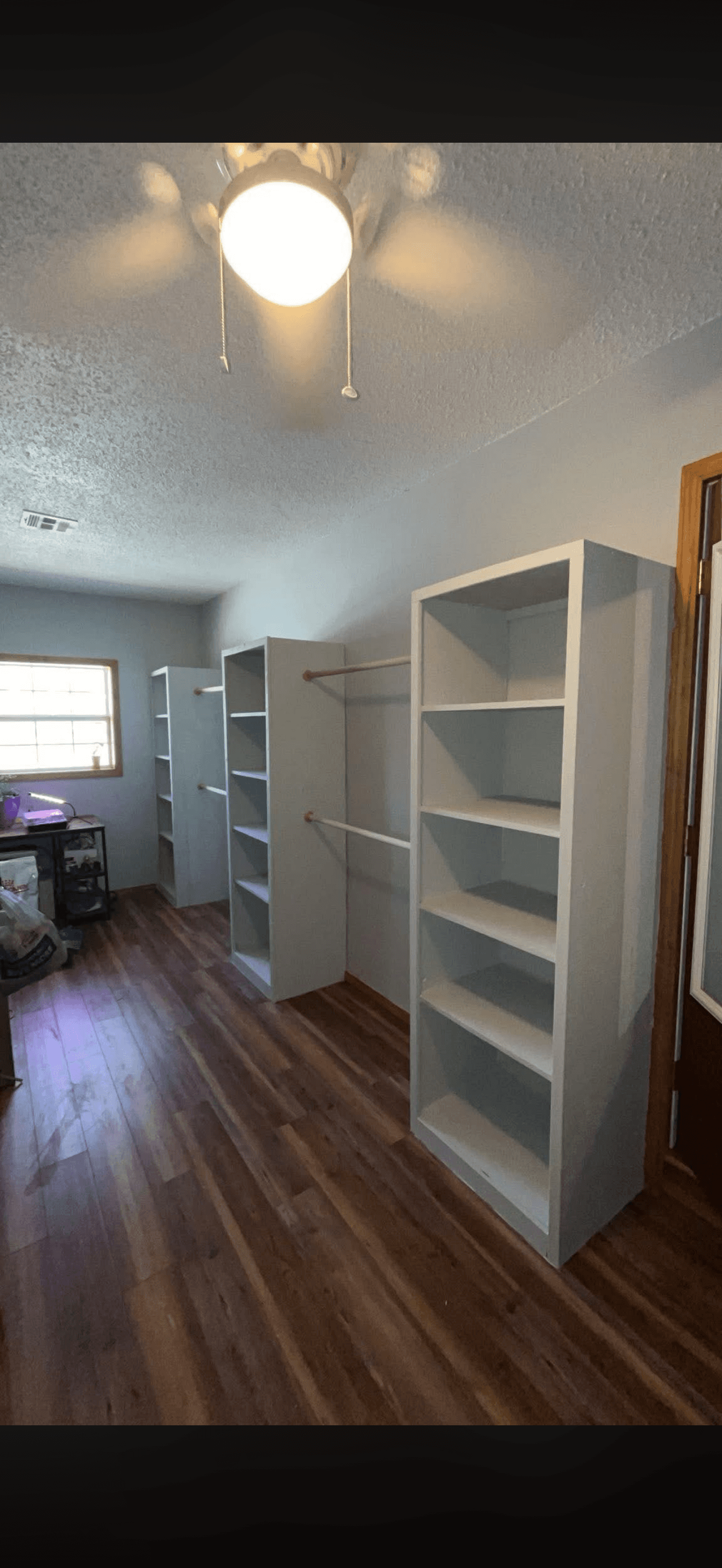 Three white shelving units with wooden hanging rods along a wall over dark wood flooring.