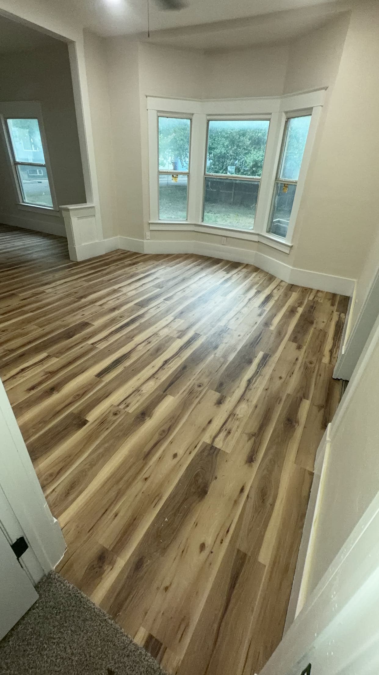 Empty room with light walls, a bay window, and multi-toned wood-look plank flooring.
