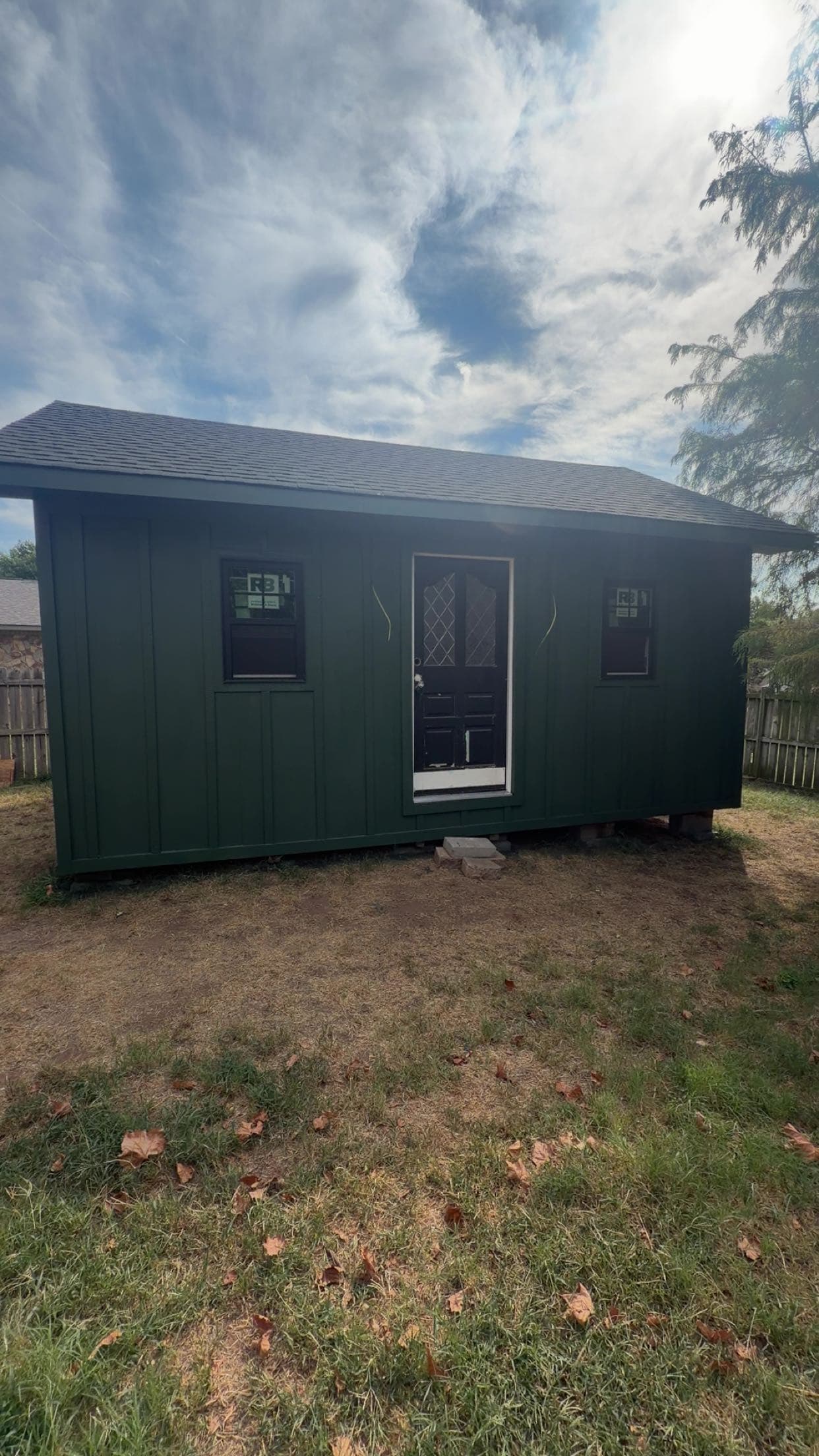 Dark green board and batten shed with two windows and a central door.