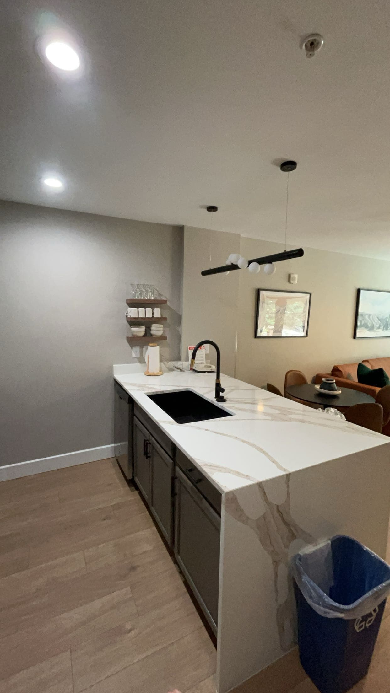 Modern kitchen island with white marble countertop, black sink, and grey cabinets in an open room.