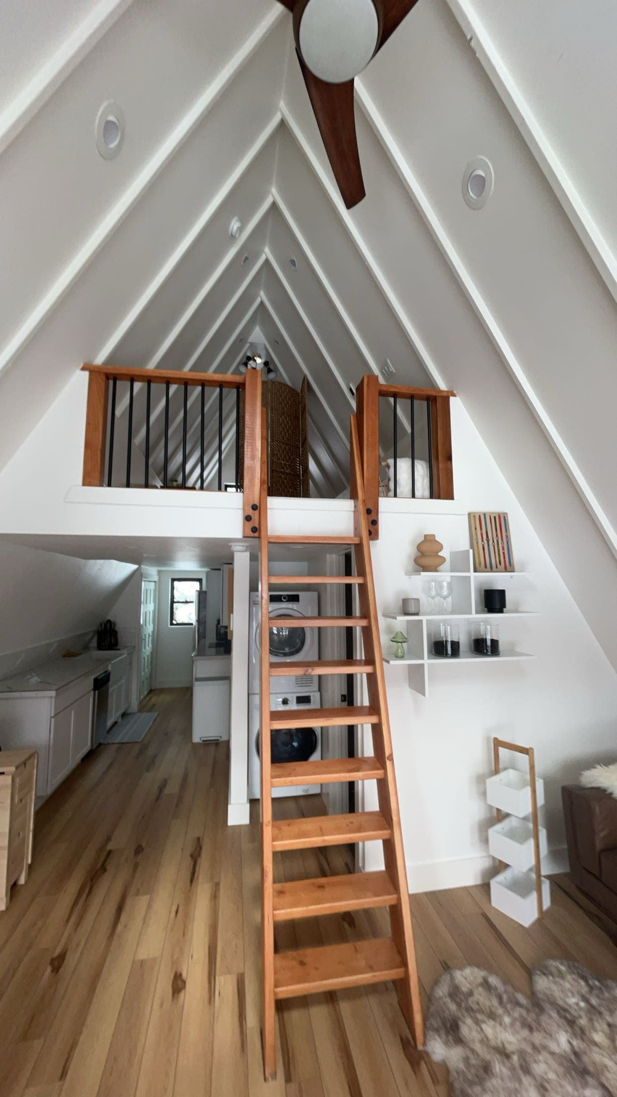 Modern A-frame cabin interior with a wooden ladder leading to a loft and laundry nook.