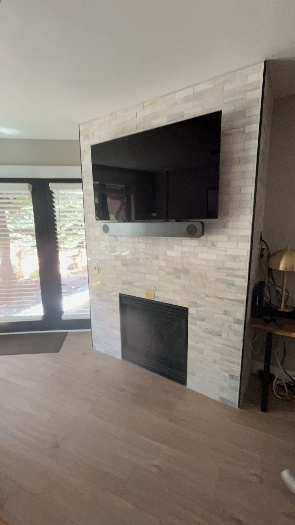 TV and soundbar mounted on a light stone wall above a black fireplace insert.